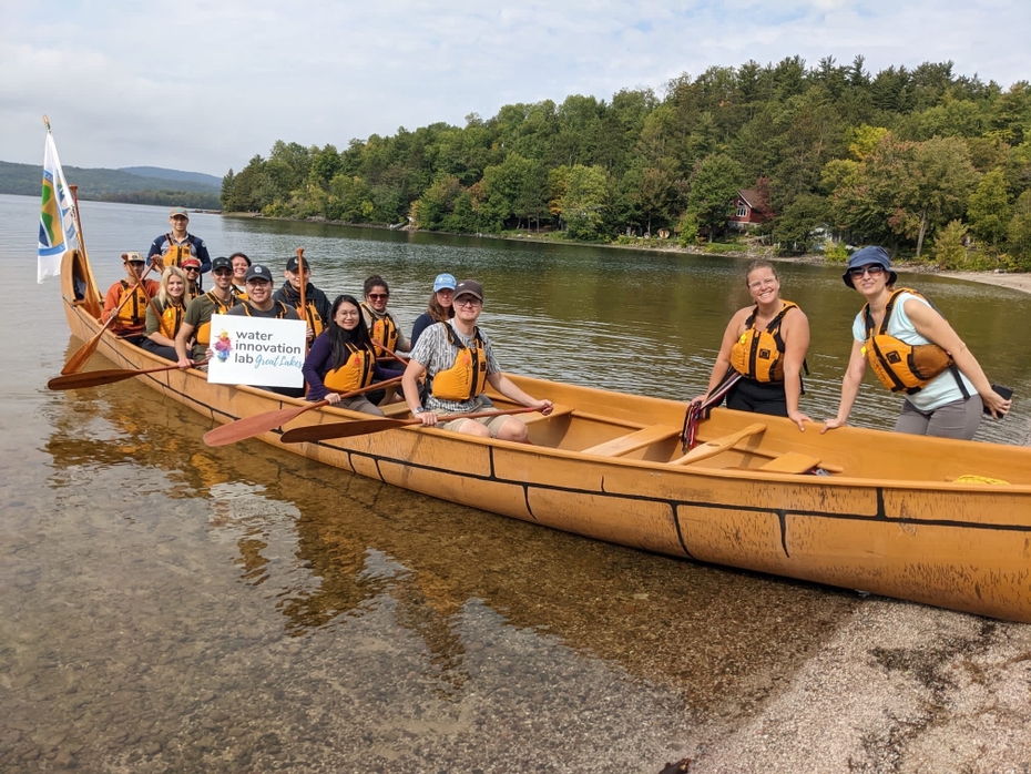 A group of students pictured in and beside a canoe in the water